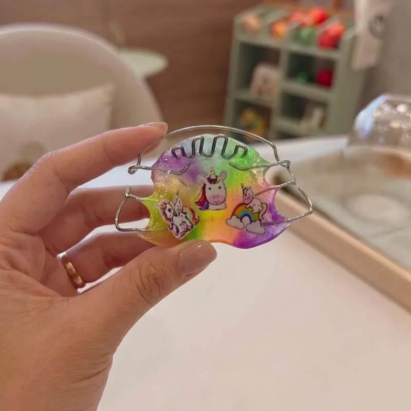 Aparelho ortopédico infantil colorido com estampa de unicórnios na mão da Dra. Aline