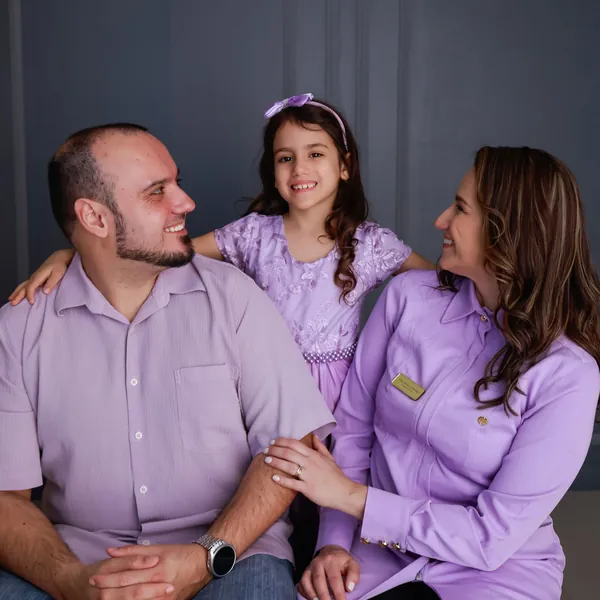 Dra. Aline sorrindo com a filha e o marido
