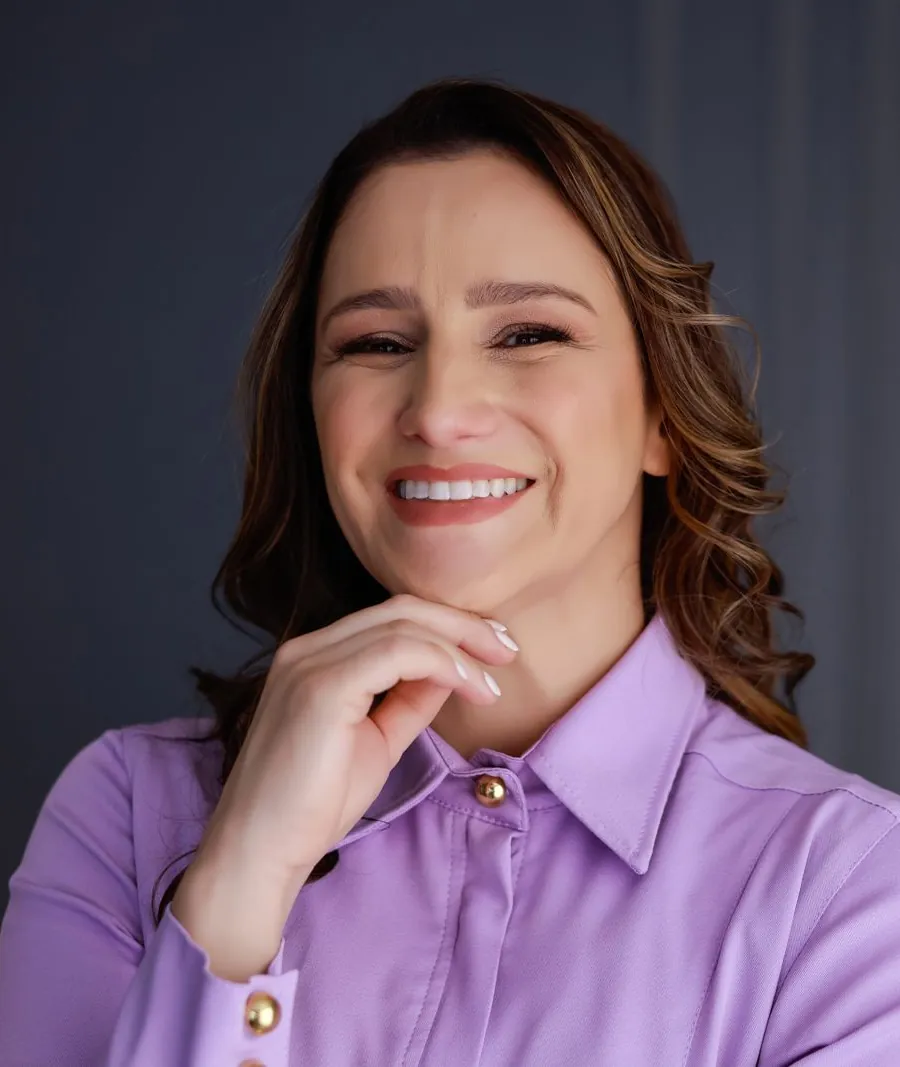 Dra. Aline Struckel sorrindo com a mão no queixo, em retrato de estúdio